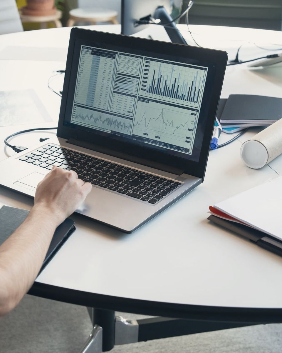 An analyst working on a laptop that shows charts and data tables at a round desk.